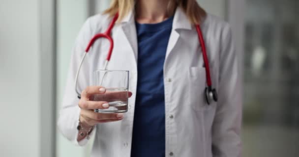 女性の医師は 水のガラスを保持する診療所の廊下に立っています セラピストは毎日十分なきれいな水を飲むことの重要性を思い出します — ストック動画