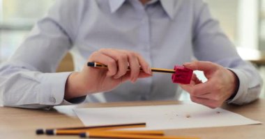 Kadın masaya oturur, elinde kalem ve bileyiciyle oturur. Dişi eller kalemi açıcıda döndürür