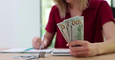 Kadın dolar tutuyor, hesap makinesindeki harcamaları sayıyor ve not defterine yazıyor. Gelir ve mali bütçe giderleri