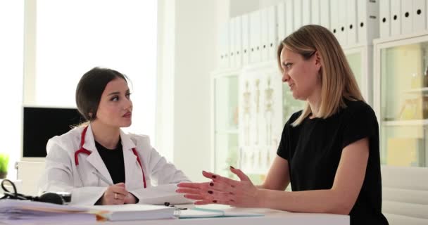 病院で女性医師に耳を傾けることに集中した若い女性患者 専門のセラピストが診療所で検査中に女性の健康保険をアドバイス — ストック動画