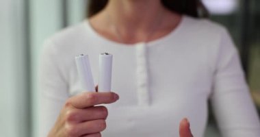 Markasız beyaz AA pil. Elinde pil ve baş parmak tutan bir kadın.