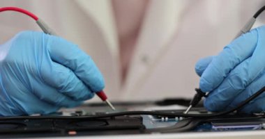 Kırık bilgisayar anakartında voltmetre kullanan eldivenli bir mühendisin elleri. Bilgisayar donanımı onarımı ve denemesi