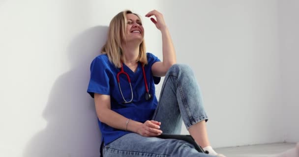 疲惫的外科医生歇斯底里地坐在诊所大厅的地板上笑着 女医生和工作中的紧张关系 — 图库视频影像