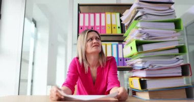 Gergin ofis çalışanı masa başında evrak yığınının arkasında oturuyor ve imzalamaya yardım ediyor. Kadın yardım ve dosya yığını ve boş belge ve başvuru istiyor