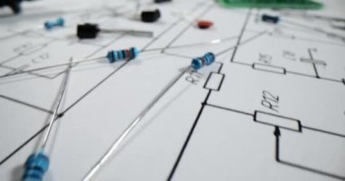 Basılı devre kartı diyagramının arka planında direnç ve kapasitörlü çeşitli elektronik parçalar veya bileşenler var. Transistörler ve geçiş devreleri