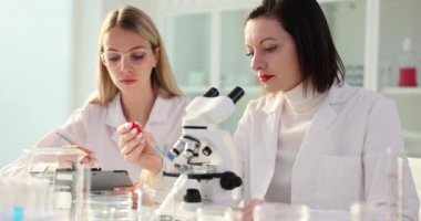 Laboratuvar teknisyeni ve bilim adamı mavi sıvıyı cam tabağa atıp mikroskoptan bakıyor. Kimyasal-tıbbi ilaç laboratuarında işbirliği