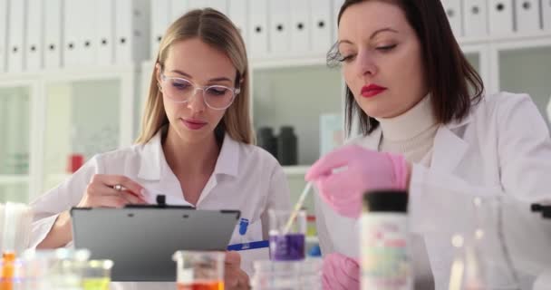 戴着手套的学生实习生和科学家在实验室里拿着装有紫色液体和试纸的瓶子 从事有毒液体或溶剂研究的妇女 — 图库视频影像