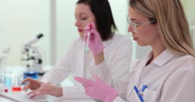 Ekip bilim adamı laboratuarda çalışıyor ve deney tüplerini sıvıyla tutuyor. Laboratuvar asistanı damlayan şeffaf cam pipetli damlatıcıyı tutuyor.