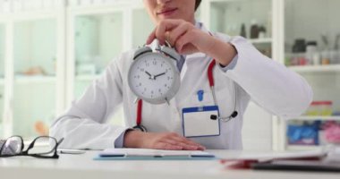 Gülümseyen kadın doktor, sağlıkla ilgilenmek ve doktoru ziyaret etmek için masaya çalar saati yerleştirir. Yavaş çekimde doktordan nazik bir hatırlatma.