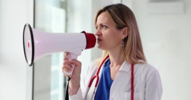 Sarışın terapist pencerenin yanında dururken hoparlöre konuşuyor. Doktor hastalara ofisten hoparlörle anons yapıyor.