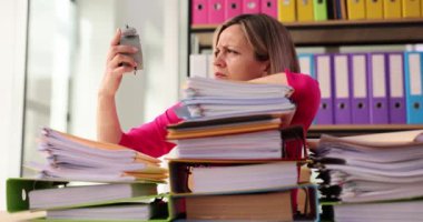 Yorgun sarışın ofis çalışanı mesai saatinin sonuna bakıyor. Uykulu kadın elinde antika çalar saatle doküman klasörleriyle dolu masada oturuyor.