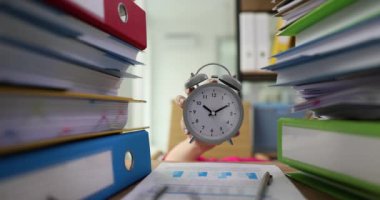 Kadın, iş yerindeki klasörler arasındaki süreyi gösteren klasik çalar saat gösteriyor. Ofis çalışanı şirket ofisinde mesai saatinin bitmesine dakikalar kaldı.