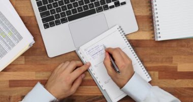 Yönetici, masadaki dizüstü bilgisayarla karşılaştırıldığında yapılacaklar listesindeki görevleri siler. Erkek çalışan, ofis iş yerindeki günlük iş akış noktalarını kontrol eder