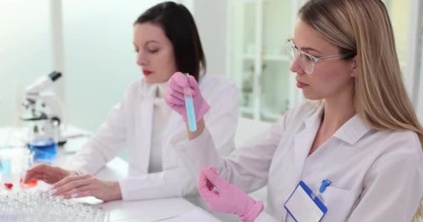 ゴム製手袋を身に着けている女性の実験室の技術者は ガラス試験管の異なる物質の化学反応の品質を評価します 化学研究所 — ストック動画