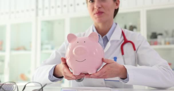 医師の手がピンクのピギーバンクを持っています 医療コンセプトへの寄付 — ストック動画
