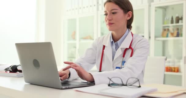 医師は病院のテーブルに座り ラップトップでオンラインで働いている コンピュータスクリーンとコンサルティング患者を中心とした看護師 — ストック動画