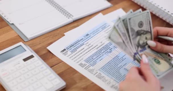 アメリカの税金 ペンとアメリカのお金の計算機 女性の手で 米国市民の机上の個々の税金形態1040 — ストック動画