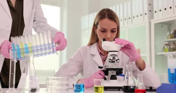 Женщина Работает Лаборатории Смотрит Микроскоп Коллега Ученый Ставит Пробирки Жидкостями — стоковое видео