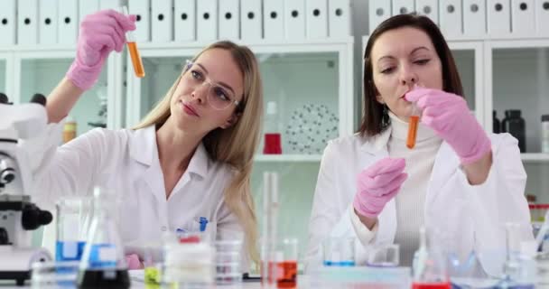 Collègue Scientifique Examine Des Éprouvettes Avec Liquide Orange Laboratoire Recherche — Video