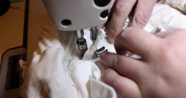 裁缝师的手握住白色的纺织品斜纹棉裤 然后在机器上缝制 工作场所现代缝纫机上的女性手缝制白色面料 — 图库视频影像
