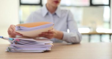 Kadın ofis çalışanı bir yığın belgeyi sıraladı. Ofis çalışanı masaya oturur ve bir yığın iş belgesini düzenler.