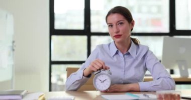 Kadın patron ya da yönetici işyerindeki çalar saati işaret ediyor. Zaman yönetimi üretkenliği artırmak için saati kullanıyor