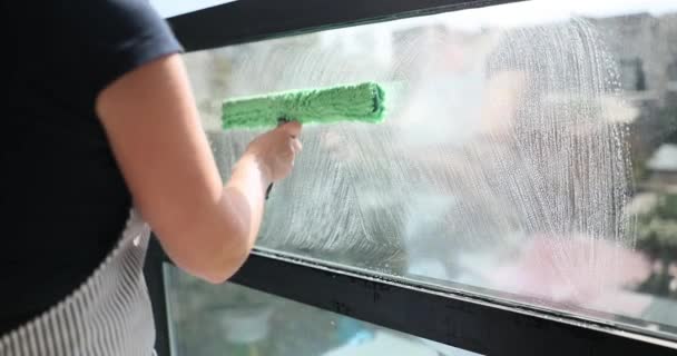 エプロンの女性は慎重にスクレーパーとスプレーヤーで窓をきれいにします 従業員は窓から水を拭くためにスプレー ボトルおよびスクイージを使用して窓を洗います — ストック動画