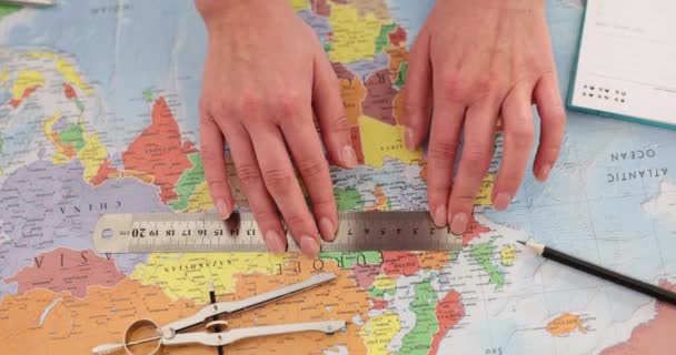 女性の手は 定規とコンパスを使用してワールドマップ上の距離を測定します ツーリストは世界地図上の距離を測定するためにルーラーを使用します — ストック動画