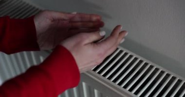 Evde merkezi ısıtma sistemi ve radyatörde kadın eli. Soğuk sonbahar kış mevsiminde ev ısıtıcısının yanında kız ellerini ısıtır.