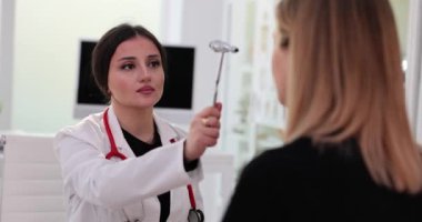 Nörolog refleksleri özel çekiçle kontrol ediyor ve genç bayan hastayı muayene ediyor. Sinir sistemi hastalıklarının teşhisi
