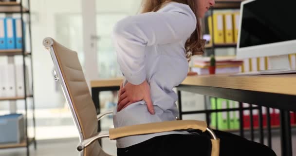 バッカチェの女性は 企業のオフィスで机に座っているウエストを伸ばします 従業員は 職場での背中の痛みと低アクティビティライフスタイルに苦しんでいます — ストック動画