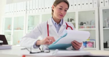 Aile doktoru hastane ofisinde kağıtları panoya asıyor. Kadın tıp uzmanı klinikteki randevusu sırasında hasta kayıtlarını kontrol ediyor. Sağlık hizmetleri