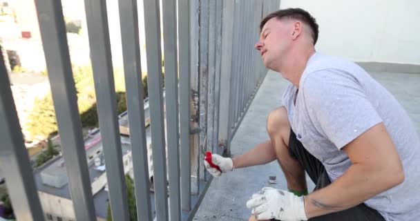 公寓主人用滚轮慢动作油漆阳台金属围栏 年轻的杂工在楼梯平台的栅栏框架上使用灰色颜料和工具 — 图库视频影像