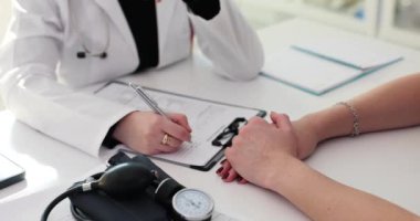 Kadın hekim hasta için tedavi planını kağıda yazıyor. Aile doktoru, ağır çekim teşhisinde merhamet göstermek için hastanın elini tutuyor.