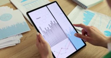 Kadın, iş yerindeki tablet üzerinde çeşitli grafik ve çizelgeleri analiz ediyor. İş kadını karmaşık detayları yavaş çekimde keşfetmek için satır ve bar çizelgelerini inceliyor
