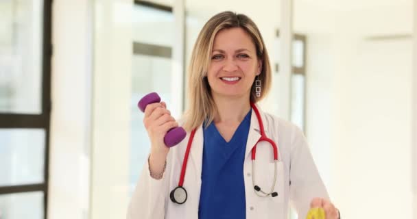 笑顔の女性医師は ダンベルと測定テープを持っています 家族の医師は 運動の重要性を強調し 測定の遅い動きを監視する — ストック動画