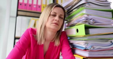 Uykucu kadın ofis çalışanı bir yığın belgenin yanında oturuyor. Yorgun yüzlü kadın, enerjiyi yavaş çekimde toplamak için ara verme ihtiyacı duyuyor.