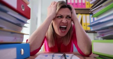 Sekreter, incelenmesi gereken büyük dosyaları değerlendirirken gözle görülür şekilde stresli görünüyor. Kadın, ağır çekimde geniş halka klasörleri ile çevrelenmiş hissediyor.