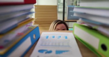 Ofis çalışanı çalışmak için yüksek klasör yığınlarına bakıyor. Kadın hayal kırıklığını yansıtıyor. Muazzam miktarda evrak işi ağır çekimde.