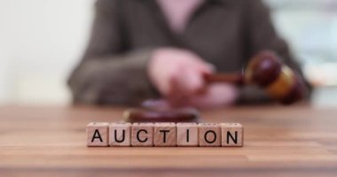 Çekiçli kadın açık arttırma masasının arkasında teklif alıyor. Müzayedeci seyirciler arasında antika eşya satışını yönetiyor. Kamu ticaret aktivitesi