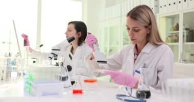 Kadın asistan, laboratuarda testler yapan çok kanallı pipetle sıvıyı tepsiye damlatıyor. Laboratuvarda çalışma materyalleri olan bir tıp teknisyeni.