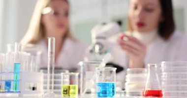 Renk sıvılarıyla dolu cam mataralar ve kimya laboratuvarında çalışan kadın bilim adamları. Tıp öğrencileri farklı materyalleri teknolojiyle test ederler.