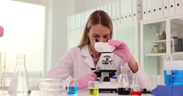 Γυναίκα Επιστήμονας Κοιτάζει Στο Μικροσκόπιο Ενώ Συνάδελφος Φέρνει Ράφι Δοκιμαστικούς — Αρχείο Βίντεο