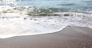 Deniz kıyısındaki ıslak kumsalda köpüklü deniz dalgaları ağır çekimde dönüyor. Gök mavisi okyanus suyu sabahları parlak güneş ışığında kıvılcım saçar. Sakin doğa sahnesi