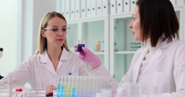 科学者は 化学実験室の若い研修生に臭いのある液体を匂わせる 女性のテクノロジストは 薬物製造のための紫の物質と協力しています — ストック動画