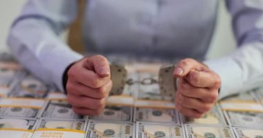 Bayan işçi, ofiste nakit parayla kaplı bir masanın üzerine kelepçeyle el kaldırıyor. Yozlaşmış iş kadını yasadışı para aklamaktan tutuklandı