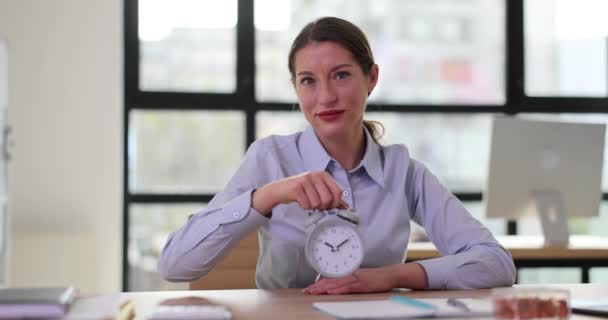 笑顔の女性マネージャーは 木製の机に座っている目覚まし時計を示しています 女性チームリーダーは 会社のオフィスの遅い動きの期限を思い出します — ストック動画