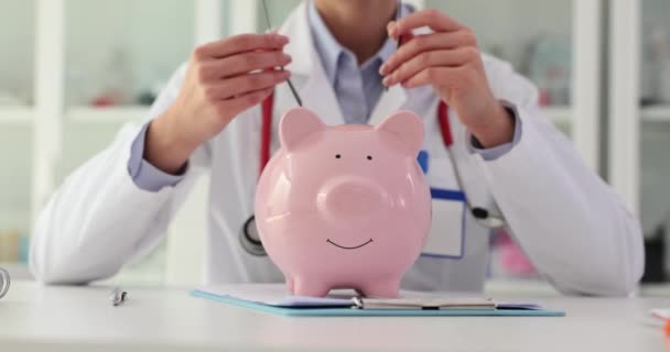 Sanitäterin Setzt Brille Auf Und Lächelt Sparschwein Auf Schreibtisch Krankenhaus — Stockvideo