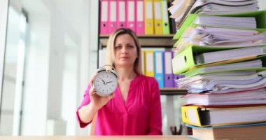 Yorgun sarışın kadın dosya yığınında oturur ve işaret parmağını çalar saatin yanında gösterir. Genç ofis çalışanı yorgunluğunu ifade ediyor ve mevcut zaman akışını gösteriyor