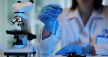 Nitelikli bilim adamı labaratuvarda mavi sıvının özelliklerini inceliyor. Araştırmacı sıvının kimyasal özelliklerini yavaş çekimde inceliyor.